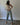 A woman models a white ribbed tank top with gold button details, light-wash blue cropped jeans, and cream pointed-toe heels against a plain white studio backdrop.