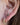 Close-up of a person's ear showing two gold piercings: a small round green gemstone stud at the lobe and a textured gold hoop at the helix.