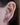 Close-up of a person's ear wearing two small gold stud earrings: one round white opal and one triangular dark green stone in a gold bezel setting.