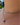 A close-up of a person's neck and collarbone wearing two layered gold necklaces. The top chain is a delicate beaded necklace with small blue beads, and the bottom chain features a gold beaded necklace with a blue and white fish pendant.
