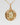 A gold pendant necklace featuring a circular, openwork geometric design with a central light green gemstone, suspended from a gold chain against a light gray background.