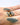 A close-up of a hand with gray tattoos wearing a gold ring with a dark blue oval gemstone, alongside two gold bands.