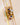 A stack of gold rings with various colored gemstones displayed on a clear glass cylinder against a warm beige background.