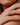 Close-up of a hand wearing a gold ring with a diamond on a neutral background
