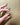 A close-up of a hand with brown nail polish holding three silver earrings against a textured tan background.