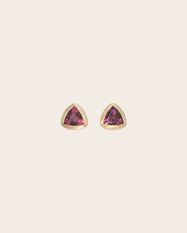 A pair of gold triangular stud earrings with pink gemstones, centered on a light beige background.